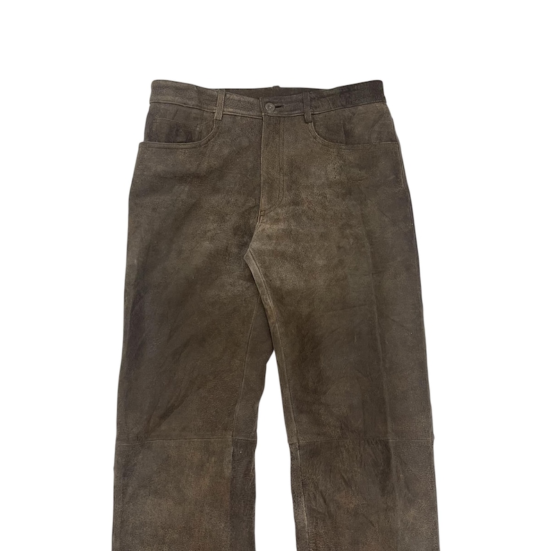 Pode incluir: Cal&ccedil;as de camur&ccedil;a castanhas com fecho de bot&atilde;o e z&iacute;per. As cal&ccedil;as t&ecirc;m dois bolsos frontais e dois bolsos traseiros. A cor neutra e o estilo cl&aacute;ssico d&atilde;o-lhe um visual casual.