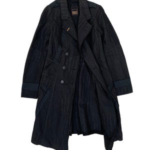 May include: Black trench coat with vertical pinstripes. The coat features a double-breasted design with four buttons, a notched collar, and a belt detail on the sleeves. The coat is open, revealing the interior lining.