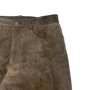 Pode incluir: Close-up de cal&ccedil;as de couro castanho. As cal&ccedil;as t&ecirc;m fecho de bot&atilde;o e um bolso. O couro tem um aspeto desgastado com varia&ccedil;&otilde;es de cor. As cal&ccedil;as s&atilde;o de cor neutra e podem ser combinadas com muitos tops diferentes.