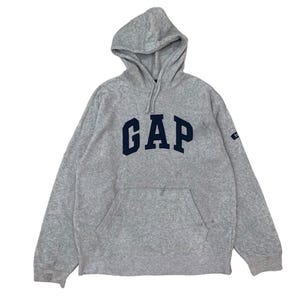 Peut inclure: Un sweat à capuche gris avec le mot "GAP" en bleu marine sur la poitrine. Le sweat-shirt a une poche avant et une petite étiquette sur la manche. Le tissu semble être une polaire douce.