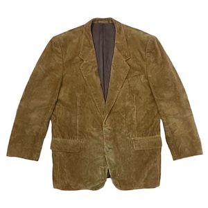 Puede incluir: Un blazer de pana color marrón con cierre de dos botones y dos bolsillos delanteros. La chaqueta tiene solapas con muescas y un forro interior marrón oscuro. Un blazer de estilo clásico.