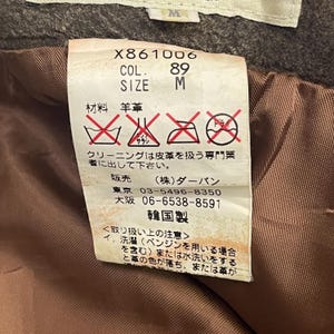 Pode incluir: Close-up de uma etiqueta de roupa com texto e s&iacute;mbolos. A etiqueta inclui o n&uacute;mero "X861006", "COL. 89" e "SIZE M". Apresenta tamb&eacute;m texto japon&ecirc;s e s&iacute;mbolos de cuidados.