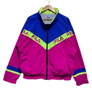 May include: A vintage Fila track jacket in a vibrant color block design. The jacket features a combination of blue, pink, and neon green. The Fila logo is printed across the chest. The jacket has a full zipper and a stand-up collar.