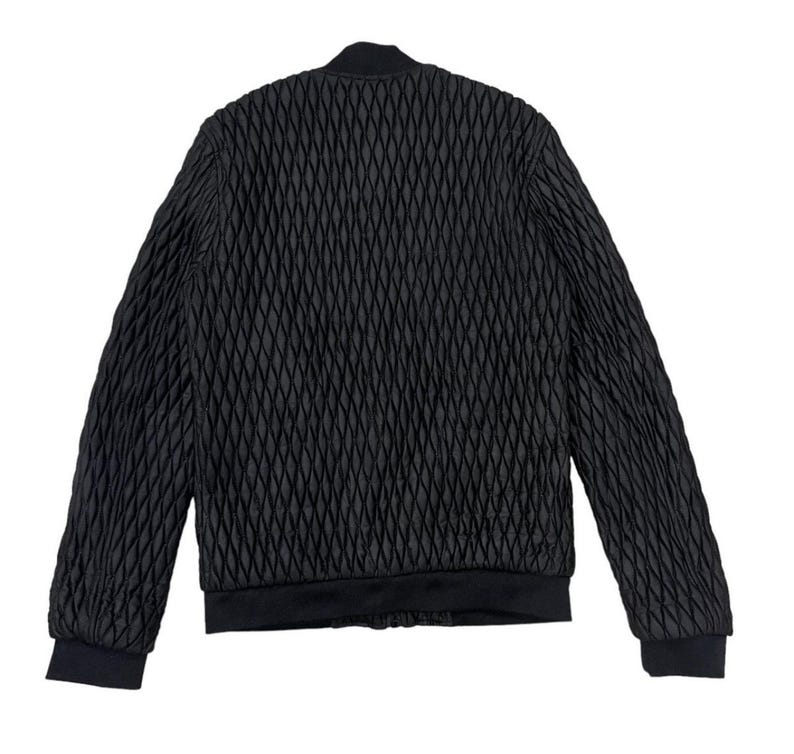 Puede incluir: Chaqueta bomber negra con un patr&oacute;n de diamantes acolchado. La chaqueta presenta cuello, pu&ntilde;os y dobladillo de canal&eacute;. La vista trasera de la chaqueta se muestra sobre un fondo blanco. La chaqueta es de color negro s&oacute;lido.