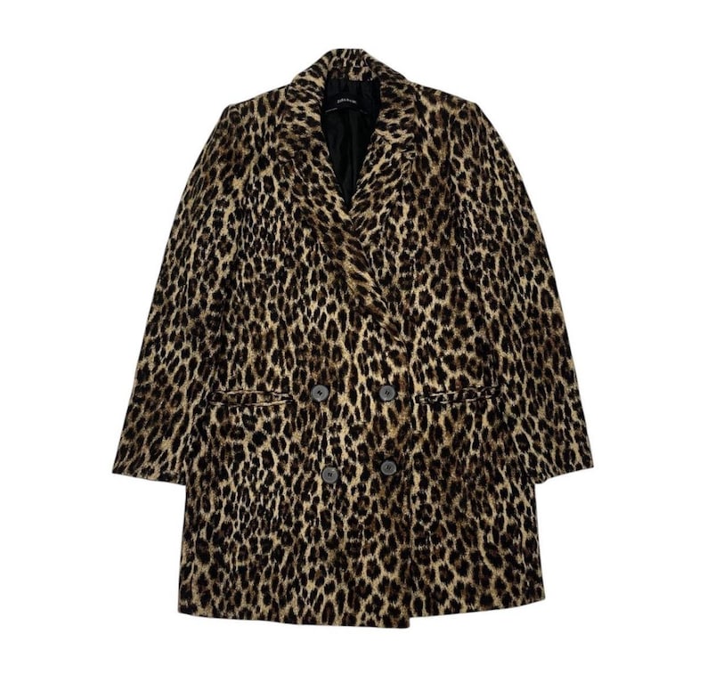 May include: A double-breasted leopard print coat in shades of brown and black. The coat features a notched collar, two front pockets, and a black lining. The coat has three dark buttons on each side.