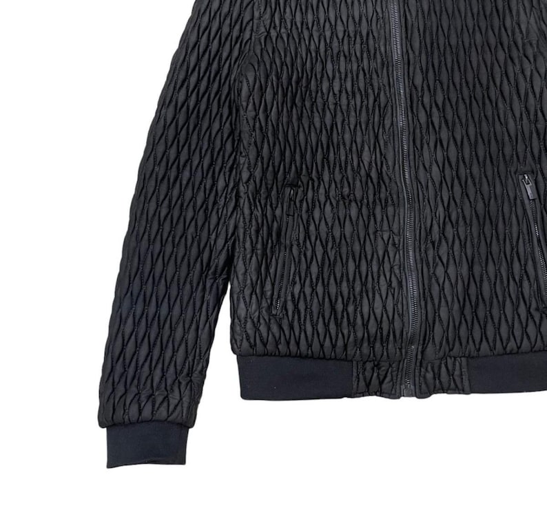 Puede incluir: Chaqueta negra acolchada con un patr&oacute;n de diamantes. La chaqueta tiene cierre de cremallera completo, dos bolsillos laterales y pu&ntilde;os y dobladillo de canal&eacute;. La tela es texturizada.