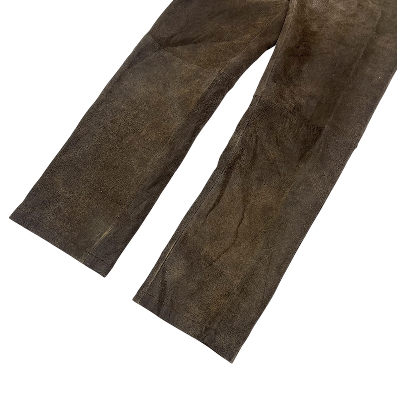 Pode incluir: Cal&ccedil;as de couro castanho com design de perna reta. As cal&ccedil;as t&ecirc;m um aspeto desgastado, com textura vis&iacute;vel e varia&ccedil;&otilde;es de cor. O couro parece macio e flex&iacute;vel.