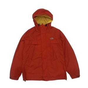 Op de afbeelding: Een rood-oranje jas met capuchon en gele binnenvoering. De jas heeft een ritssluiting aan de voorkant, twee voorzakken en het North Face-logo op de borst. Deze outdoorjas is ontworpen om te beschermen tegen de elementen.