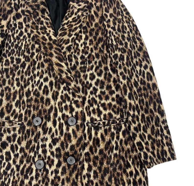 May include: A double-breasted leopard print blazer in shades of brown and black. The jacket features a notched lapel, two rows of buttons, and two front pockets. The fabric has a textured appearance.