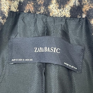 May include: Close-up of a leopard print jacket lining. The black lining has a textured pattern. A black label reads "ZARA BASIC" with sizing information and "MADE IN SPAIN".