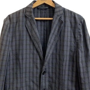 May include: A gray and blue plaid blazer with a notched lapel and two-button closure. The jacket is hanging on a wooden hanger. The blazer has a classic, tailored design.