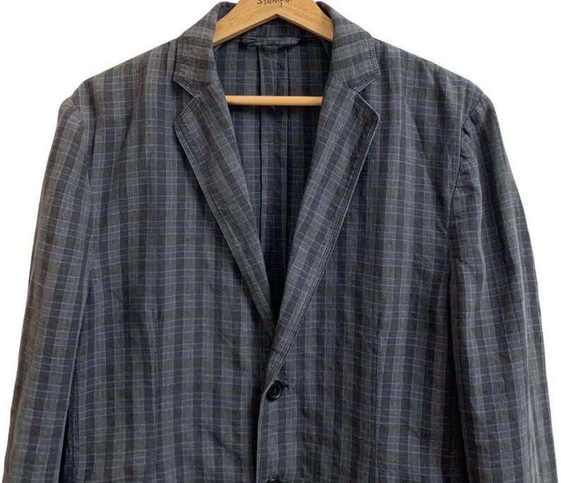 May include: A gray and blue plaid blazer with a notched lapel and two-button closure. The jacket is hanging on a wooden hanger. The blazer has a classic, tailored design.