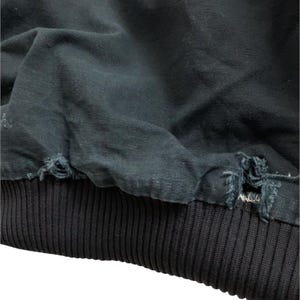 May include: Close-up of a dark navy blue jacket with a ribbed black cuff. The jacket's fabric shows signs of wear and tear, with frayed edges near the cuff. The cuff is a thick, ribbed knit.