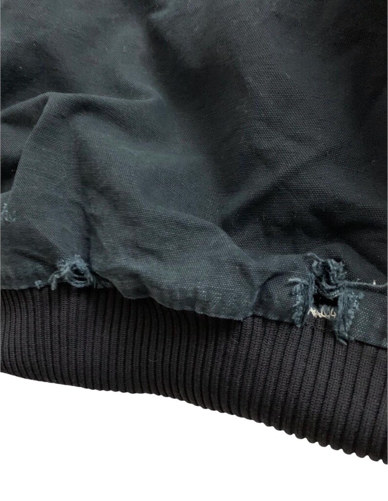 May include: Close-up of a dark navy blue jacket with a ribbed black cuff. The jacket's fabric shows signs of wear and tear, with frayed edges near the cuff. The cuff is a thick, ribbed knit.