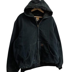 May include: Black hooded zip-up jacket with two front pockets and a ribbed hem. The jacket has a distressed area on the hood and a small logo patch. The jacket is hanging on a wooden hanger.