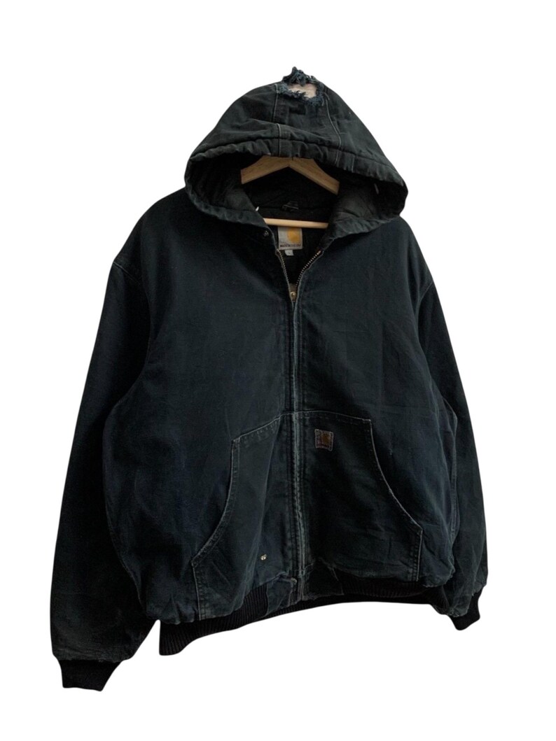 May include: Black hooded zip-up jacket with two front pockets and a ribbed hem. The jacket has a distressed area on the hood and a small logo patch. The jacket is hanging on a wooden hanger.