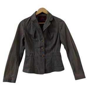 Pode incluir: Um blazer cinza escuro com um design clássico, com gola entalhada, fecho de três botões e dois bolsos frontais. O casaco está pendurado num cabide de madeira. O tecido parece ter um aspeto ligeiramente gasto ou desbotado.