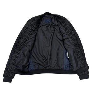 Puede incluir: Chaqueta bomber negra con un dise&ntilde;o acolchado en las mangas y los hombros. La chaqueta tiene un forro negro y cuello y pu&ntilde;os de canal&eacute;. La chaqueta est&aacute; abierta, revelando el interior.