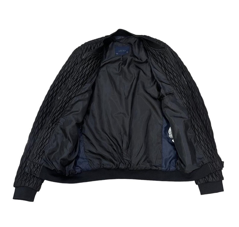 Puede incluir: Chaqueta bomber negra con un dise&ntilde;o acolchado en las mangas y los hombros. La chaqueta tiene un forro negro y cuello y pu&ntilde;os de canal&eacute;. La chaqueta est&aacute; abierta, revelando el interior.
