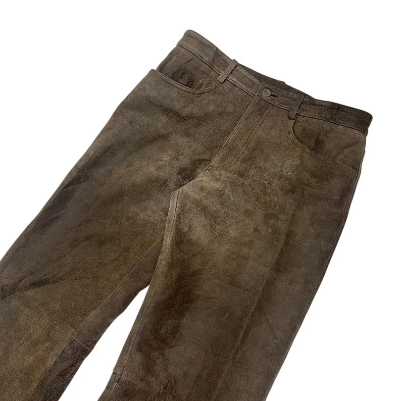 Pode incluir: Um par de cal&ccedil;as de couro castanho com um design cl&aacute;ssico de cinco bolsos. As cal&ccedil;as t&ecirc;m fecho de bot&atilde;o e z&iacute;per e presilhas para cinto. O couro tem uma apar&ecirc;ncia desgastada e texturizada.