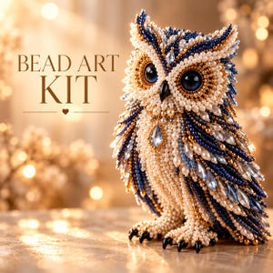 Peut inclure: Une figurine de chouette décorative faite de perles complexes dans des tons bleu marine, crème et or, avec de grands yeux sombres et des accents de cristal clair. Le texte BEAD ART KIT est affiché à gauche de la chouette en police serif.