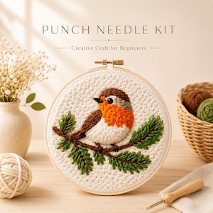 Peut inclure: Un kit de punch needle comprenant un tambour à broder en bois rond avec un motif texturé représentant un petit oiseau à tête brune, poitrine orange et ventre blanc, perché sur une branche de pin verte sur un tissu couleur crème.