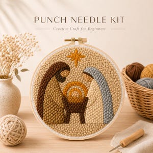 May include: A punch needle kit featuring a circular wooden embroidery hoop with a textured nativity scene design. The design depicts two figures in brown and light blue robes standing over a central manger, topped with a yellow star.