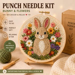 Op de afbeelding: Een punch needle kit met een ronde houten borduurring met een textuurrijk beige konijn omringd door kleurrijke bloemen in roze, geel, wit en paars. De kit bevat een houten punch needle gereedschap en groene wol.