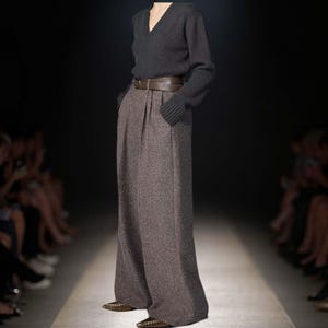 May include: A dark charcoal gray V-neck long-sleeve sweater paired with high-waisted, wide-leg brown tweed trousers. The trousers feature a brown leather belt with a buckle at the waist and are worn with pointed-toe metallic shoes.