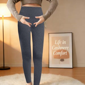 May include: Dark grey ribbed leggings. The high-waisted trousers are made of a soft material. The image includes a framed print with the text "Life in Cashmere Comfort".