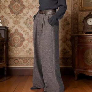 May include: A charcoal gray V-neck long-sleeve sweater paired with high-waisted, wide-leg brown tweed trousers featuring front pleats and a dark brown leather belt with a silver buckle, worn with pointed-toe dark gray shoes.