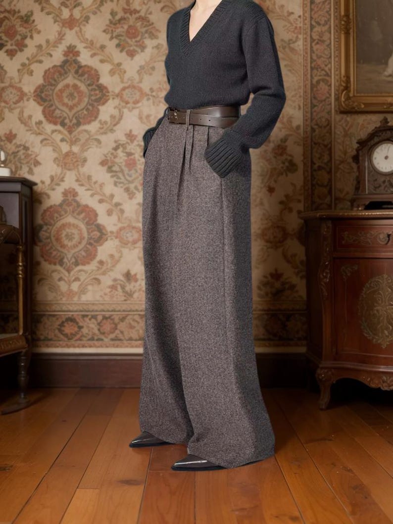 May include: A charcoal gray V-neck long-sleeve sweater paired with high-waisted, wide-leg brown tweed trousers featuring front pleats and a dark brown leather belt with a silver buckle, worn with pointed-toe dark gray shoes.