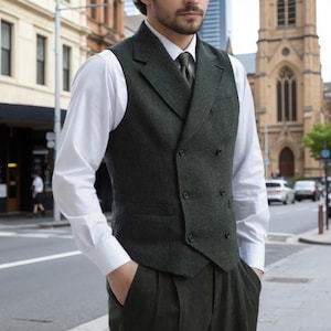 May include: A dark green tweed vest with a double-breasted design, paired with matching trousers and a white dress shirt. The vest has a notched lapel and four buttons. The outfit is completed with a green tie. The person is standing on a city street.