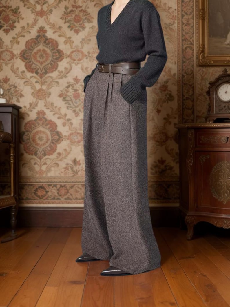 May include: A charcoal gray V-neck long-sleeve sweater paired with high-waisted, wide-leg brown tweed trousers featuring front pleats and a dark brown leather belt with a silver buckle, worn with pointed-toe dark gray shoes.