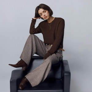 May include: A dark brown long-sleeved crewneck sweater paired with wide-leg tweed trousers in a speckled gray and brown pattern. The outfit includes a brown leather belt with a gold buckle and dark brown leather ankle boots with block heels.