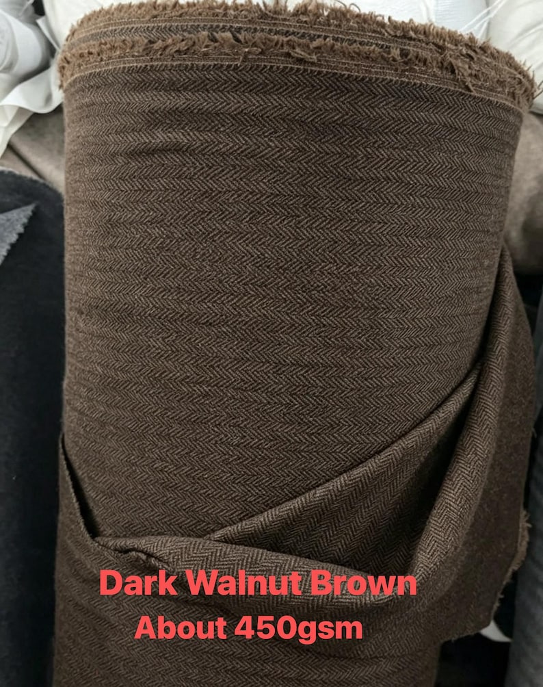 May include: A roll of dark walnut brown fabric featuring a woven herringbone pattern. The textile has a visible frayed top edge and includes printed text stating Dark Walnut Brown and About 450gsm on the lower portion of the material.