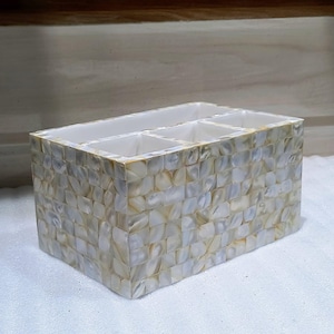 May include: Rectangular organizer with four compartments. The exterior is covered in small, square, iridescent shell pieces, creating a mosaic effect. The interior is white. The organizer is designed to hold small items.