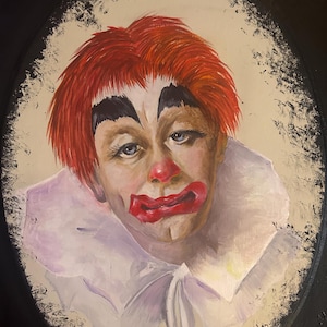 May include: Oval painting of a clown's face with red hair, a red nose, and red lips. The clown wears white makeup around the eyes and a white ruffled collar. The painting is signed "Mackie '93".