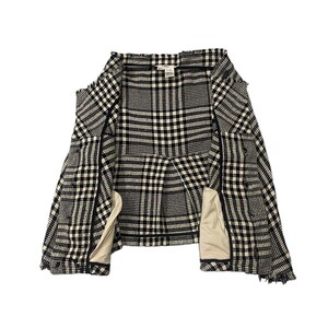 May include: A black and white plaid jacket with a classic pattern. The jacket is open, revealing a beige lining and a structured design. The fabric has a textured appearance, and the overall style is tailored.