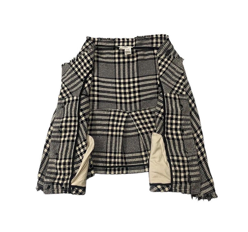 May include: A black and white plaid jacket with a classic pattern. The jacket is open, revealing a beige lining and a structured design. The fabric has a textured appearance, and the overall style is tailored.