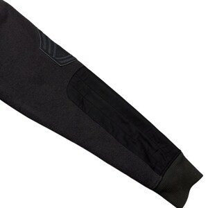 May include: Close-up of a dark grey sleeve with black patches and a ribbed cuff. The sleeve features a textured knit fabric and a patch on the upper arm with a subtle design. The black patches provide contrast.