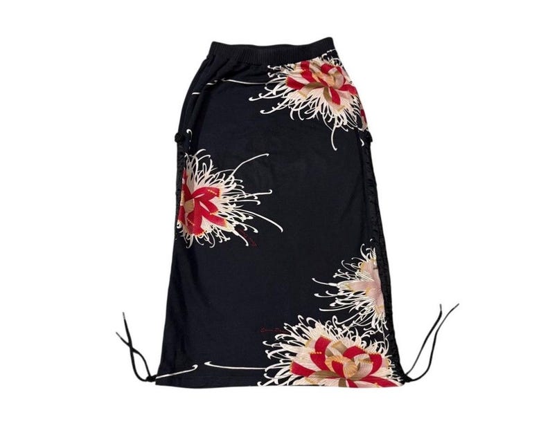 May include: Black skirt with a floral pattern featuring red, white, and tan flowers. The skirt has a drawstring waist and a flowing design. The floral print is a prominent design element, adding a touch of elegance to the garment.