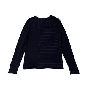 Puede incluir: Una camisa de manga larga azul marino con un dise&ntilde;o &uacute;nico. La camisa presenta un patr&oacute;n de rayas verticales en el lado izquierdo y rayas horizontales en el lado derecho. Las mangas tienen pu&ntilde;os acanalados.