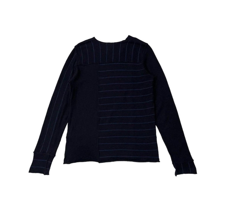 Puede incluir: Una camisa de manga larga azul marino con un dise&ntilde;o &uacute;nico. La camisa presenta un patr&oacute;n de rayas verticales en el lado izquierdo y rayas horizontales en el lado derecho. Las mangas tienen pu&ntilde;os acanalados.