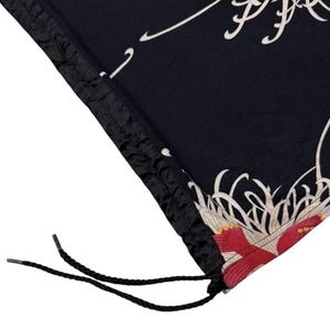 May include: Black fabric with a floral design featuring red and white accents. The fabric has a drawstring closure with black cords. The design includes white, flowing lines and a red floral pattern.