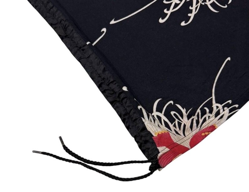May include: Black fabric with a floral design featuring red and white accents. The fabric has a drawstring closure with black cords. The design includes white, flowing lines and a red floral pattern.