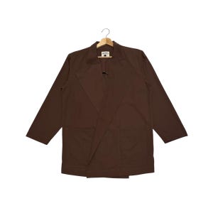 May include: A solid dark brown blazer featuring wide lapels, long sleeves, and two large front patch pockets. The garment is displayed on a wooden hanger and includes a small white rectangular brand label at the inner neckline.
