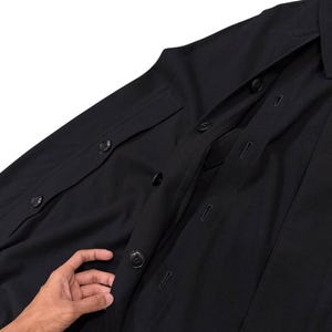 May include: A black button-down shirt with a classic collar and two chest pockets. The shirt has multiple buttons down the front and on the cuffs. The fabric appears to be a medium-weight material.