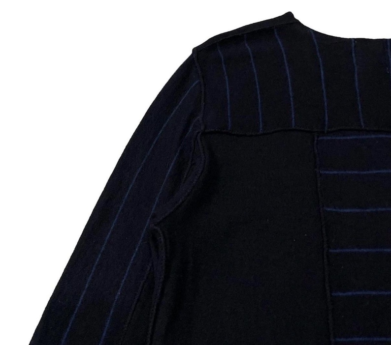 Puede incluir: Primer plano de una prenda negra con finas rayas azules. La tela parece ser un tejido de punto o tejido texturizado. El dise&ntilde;o incluye una secci&oacute;n de tela negra lisa y una secci&oacute;n con rayas azules verticales.