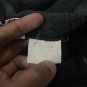 Puede incluir: Primer plano de una tela gris oscuro con una etiqueta blanca. La etiqueta tiene texto japon&eacute;s y el n&uacute;mero "RP-050120". La tela parece ser un material suave, posiblemente algod&oacute;n o una mezcla.